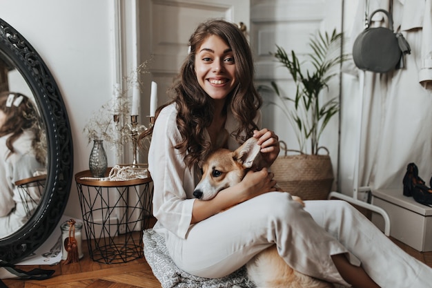 Mulher encaracolada de camisa branca se divertindo com o cachorro