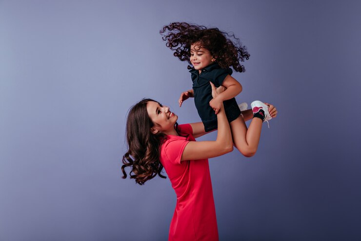Foto grátis mulher encaracolada inspirada brincando com a irmã mais nova. maravilhosa jovem mãe aproveitando o tempo de lazer com a filha.