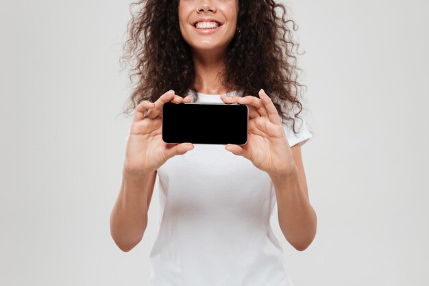 Mulher encaracolada sorridente, mostrando a tela do smartphone em branco