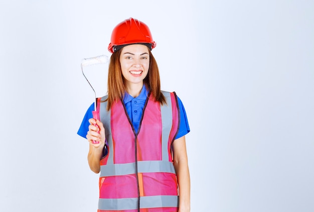 Mulher engenheira de uniforme segurando um rolo de pintura de cor branca.