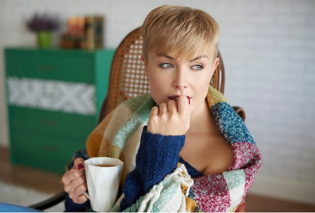 Mulher enrolada em um cobertor tomando chá quente