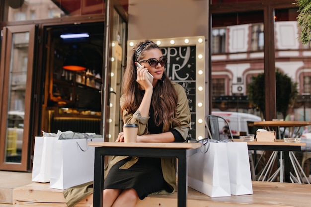 Mulher entediada ligando para alguém sentada em um café ao ar livre depois de fazer compras