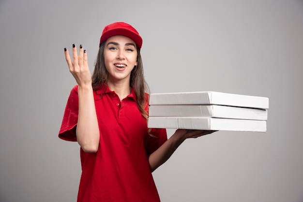 Mulher entregadora segurando pizzas na parede cinza.