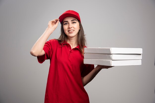 Mulher entregadora segurando pizzas na parede cinza.