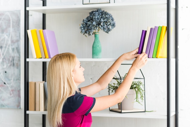 Mulher escolhendo um livro da prateleira em casa