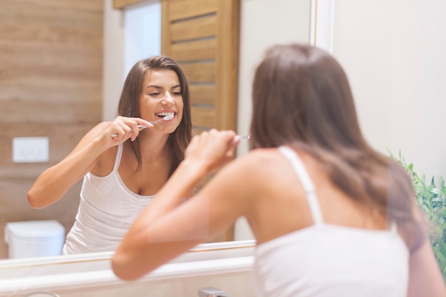 Mulher escovando os dentes na frente do espelho. Foto tirada através de vidro