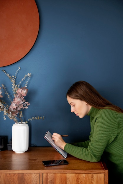 Mulher escrevendo algo em um caderno ao lado do smartphone