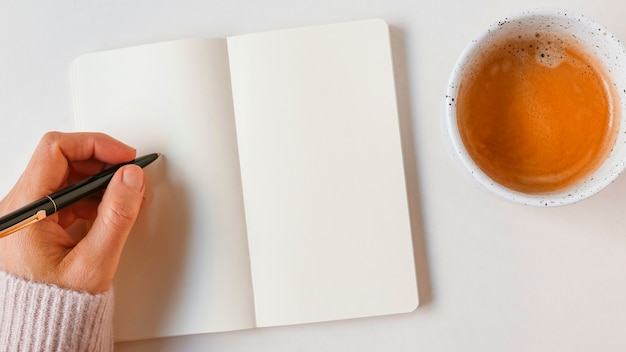 Mulher escrevendo com caneta no caderno em branco com café sobre fundo branco