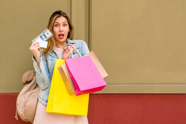 Foto grátis mulher espantada permanente com sacos de compras e dinheiro