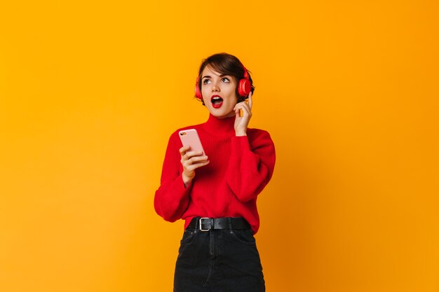 Mulher espantada posando com fones de ouvido e smartphone