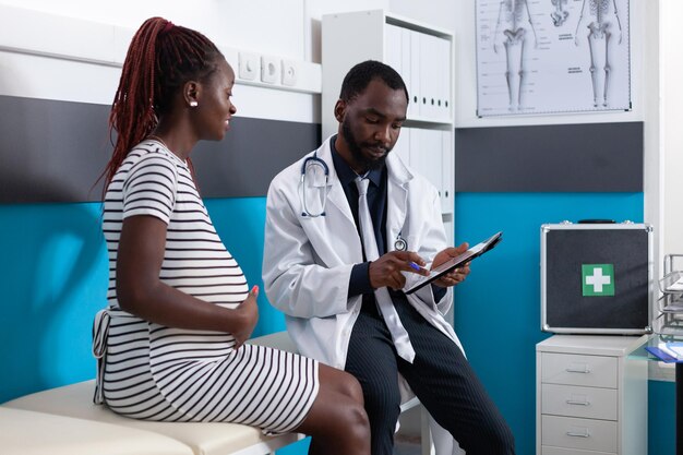 Mulher esperando filho e fazendo exame com médico no consultório médico. Clínico geral consultando paciente grávida para verificar os cuidados de saúde da gravidez. Médico ajudando a mãe