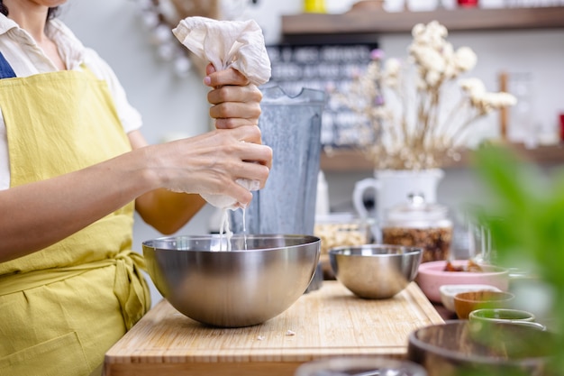 Mulher espremendo leite de amêndoa na cozinha de casa