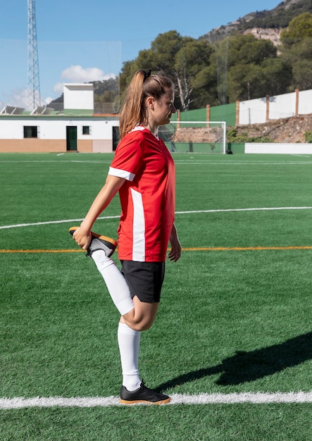 Mulher esticando a perna no campo de futebol