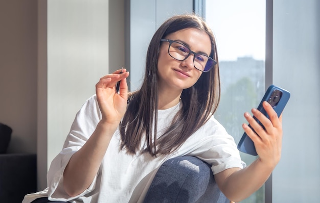 Mulher estudante com smartphone e blocos de notas na janela pela manhã