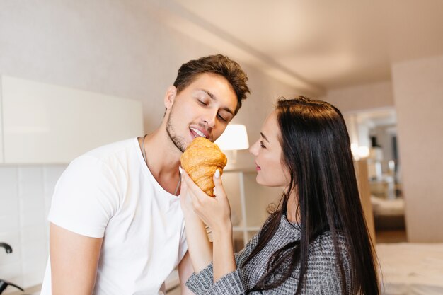 Mulher europeia de cabelos compridos alimentando namorado barbudo com croissant