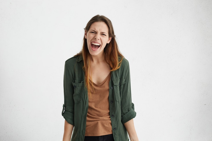 Foto grátis mulher européia furiosa com cabelo liso vestindo jaqueta verde gritando em desespero, tendo mau humor, expressando sua irritação enquanto franzia a testa e seu rosto estava isolado