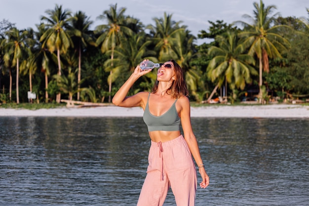 Mulher europeia jovem bonita feliz com uma garrafa de plástico de água na mão na praia