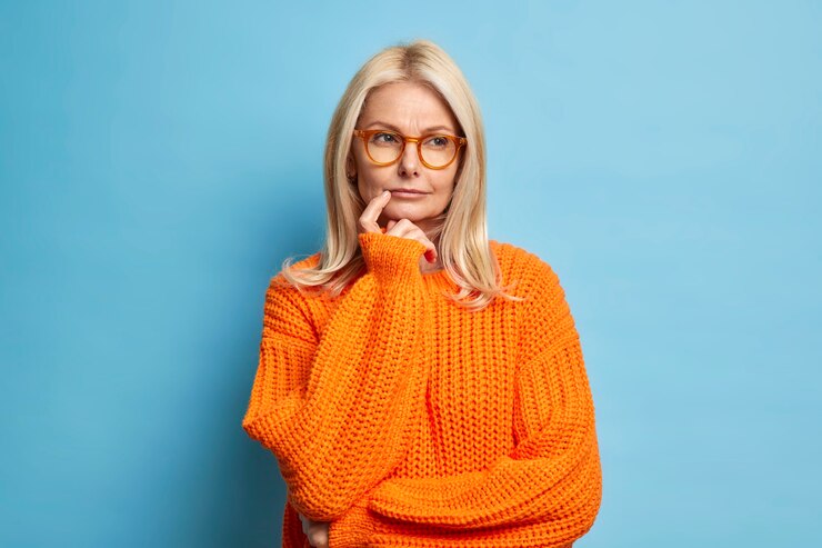 Foto grátis mulher europeia séria parece considerar pensativamente a ideia decide sobre algo tinha dúvidas vestido com um macacão de malha laranja