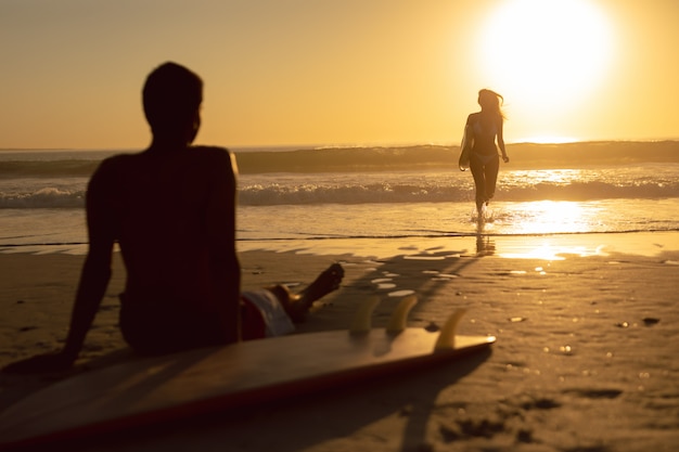 Mulher, executando, com, surfboard, enquanto, homem, relaxante, praia