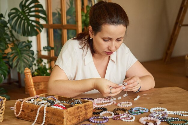 Mulher faz contas de pedras preciosas feitas à mão em sua oficina doméstica