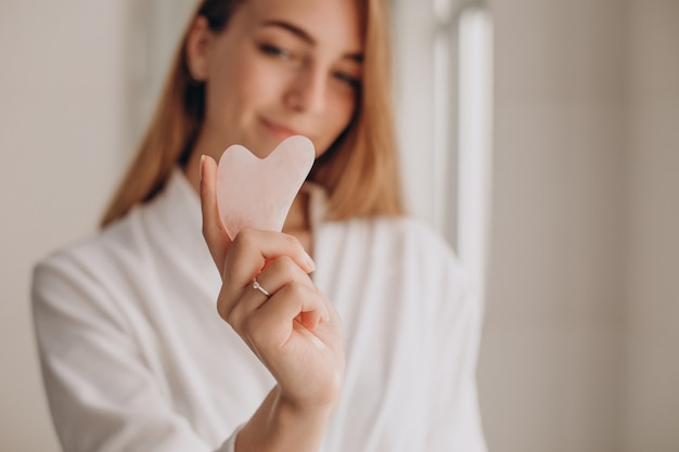 Mulher fazendo automassagem com pedra gua sha de quartzo rosa