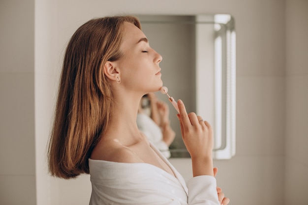 Mulher fazendo automassagem com rolo facial de quartzo rosa