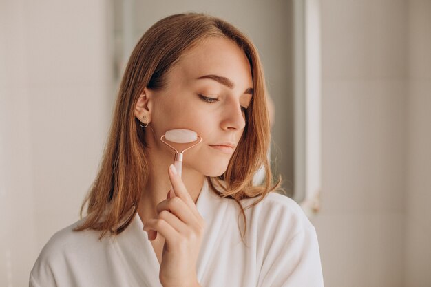 Mulher fazendo automassagem com rolo facial de quartzo rosa