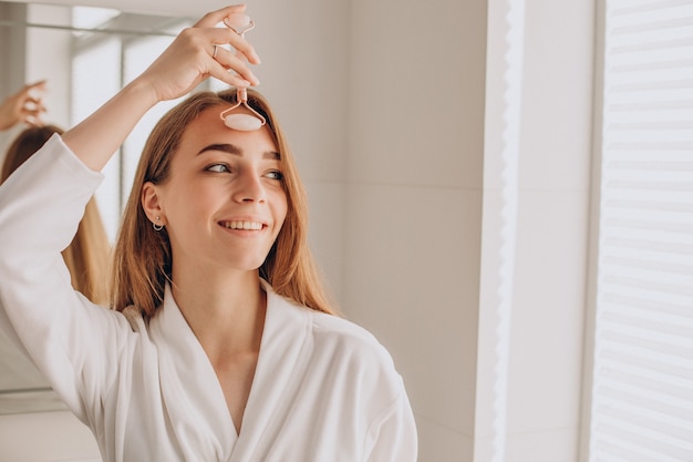 Mulher fazendo automassagem com rolo facial de quartzo rosa