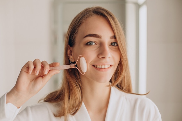 Mulher fazendo automassagem com rolo facial de quartzo rosa