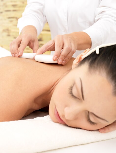 Mulher fazendo massagem com pedras quentes no corpo em salão de beleza