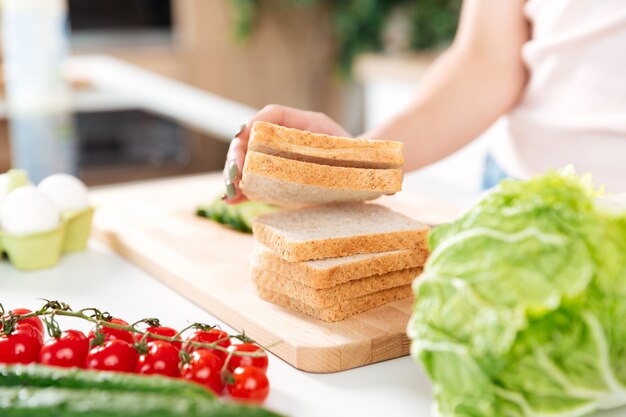Mulher fazendo sanduíches com legumes em uma placa de corte