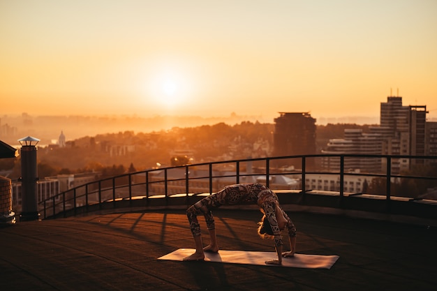 Mulher fazendo yoga no telhado de um arranha-céu na cidade grande.
