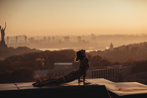 Mulher fazendo yoga no telhado de um arranha-céu na cidade grande.