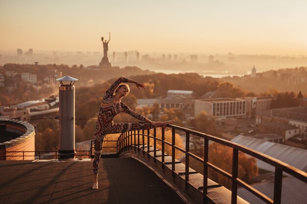 Mulher fazendo yoga no telhado de um arranha-céu na cidade grande