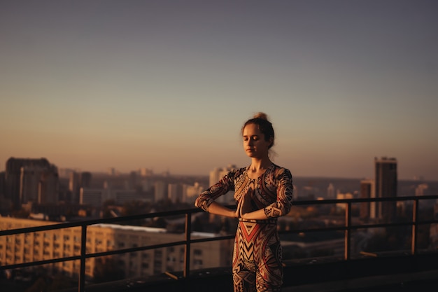 Mulher fazendo yoga no telhado de um arranha-céu na cidade grande.