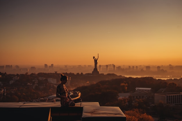 Mulher fazendo yoga no telhado de um arranha-céu na cidade grande.