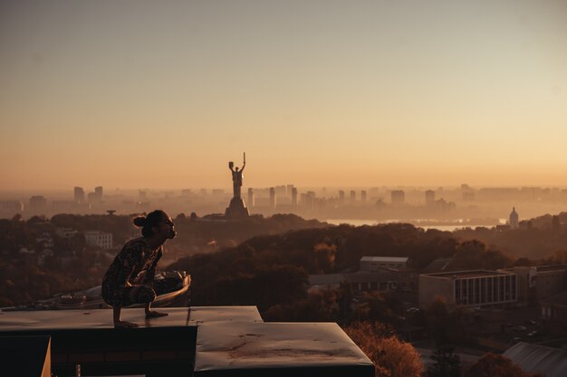 Mulher fazendo yoga no telhado de um arranha-céu na cidade grande.