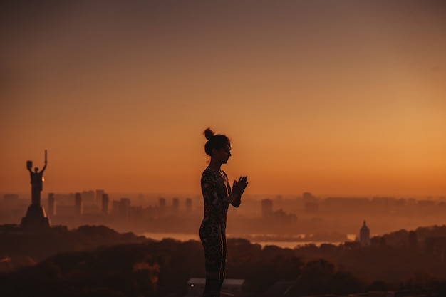 Mulher fazendo yoga no telhado de um arranha-céu na cidade grande.