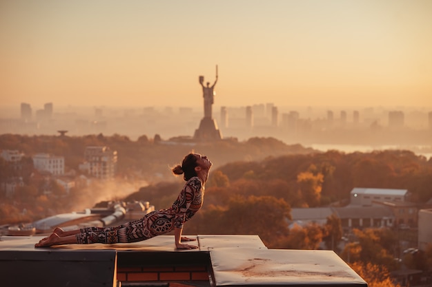 Mulher fazendo yoga no telhado de um arranha-céu na cidade grande.