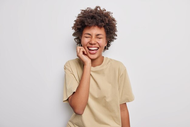 mulher fecha os olhos de felicidade ri com alegria ouve algo engraçado usa camiseta casual bege isolada no branco. Conceito de emoções e sentimentos sinceros de pessoas