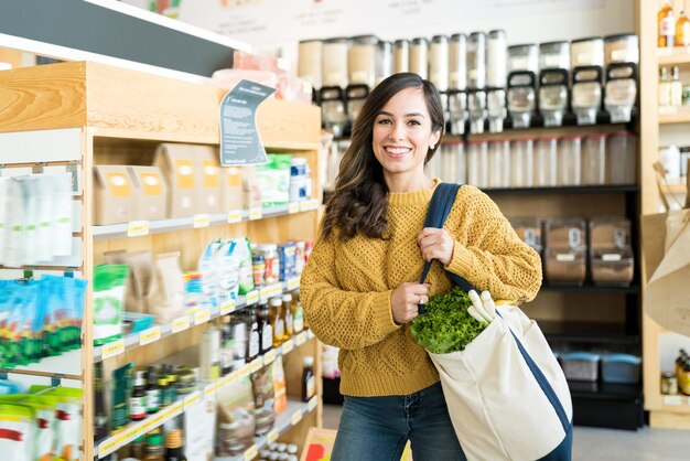 Mulher feliz carregando legumes na bolsa no supermercado