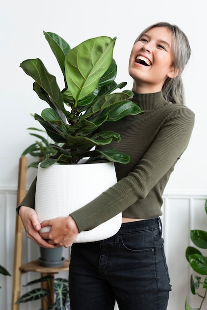 Foto grátis mulher feliz carregando uma planta de casa