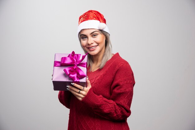 Mulher feliz com chapéu de Papai Noel, oferecendo o presente de Natal.