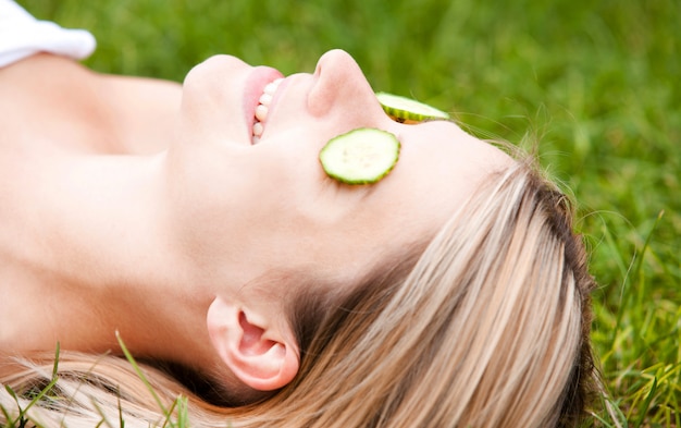 Mulher feliz com fatias de pepino no rosto