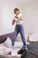 Foto grátis mulher feliz com roupas casuais em casa no quarto ouvindo música em fones de ouvido, dançando e pulando