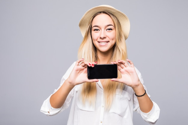 Mulher feliz com roupas casuais, mostrando a tela do smartphone em branco sobre a parede cinza