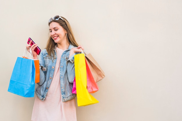 Mulher feliz com sacos de compras usando smartphone