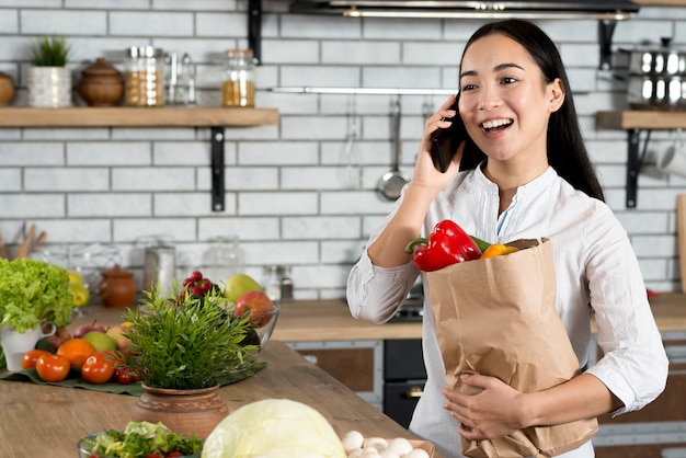 Mulher feliz, com, telefone móvel, segurando, marrom, legumes, saco