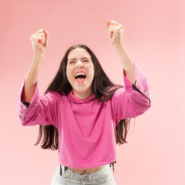 Foto grátis mulher feliz de sucesso vitorioso comemorando ser um vencedor. imagem dinâmica do modelo feminino caucasiano no fundo rosa do estúdio.