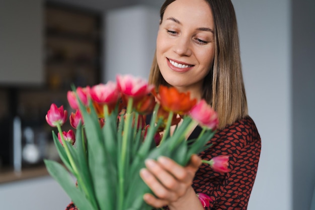 Mulher feliz desfruta de buquê de tulipas dona de casa desfrutando de um monte de flores e interior da cozinha doce lar sem alergia